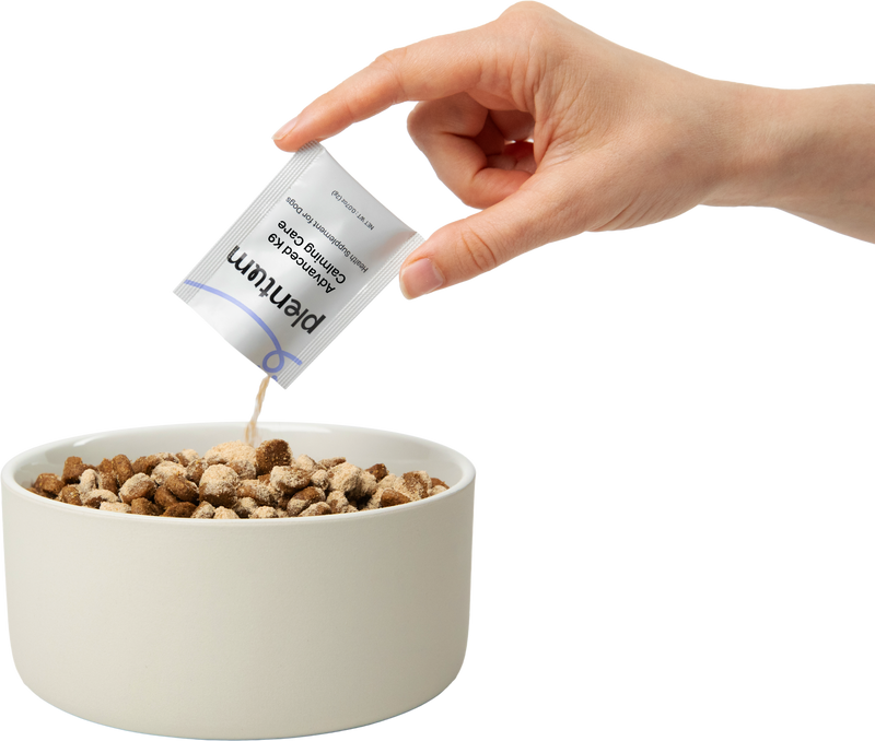 Hand pouring a Plentum Calming Care sachet of calming powder over dog kibble